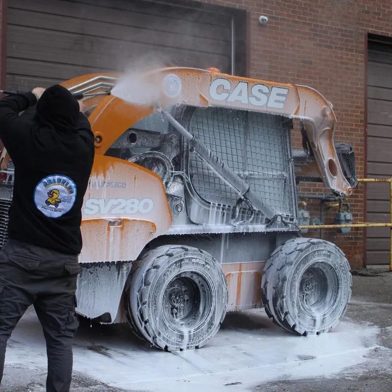A Sparkles detailer foam-washing a CASE skid steer